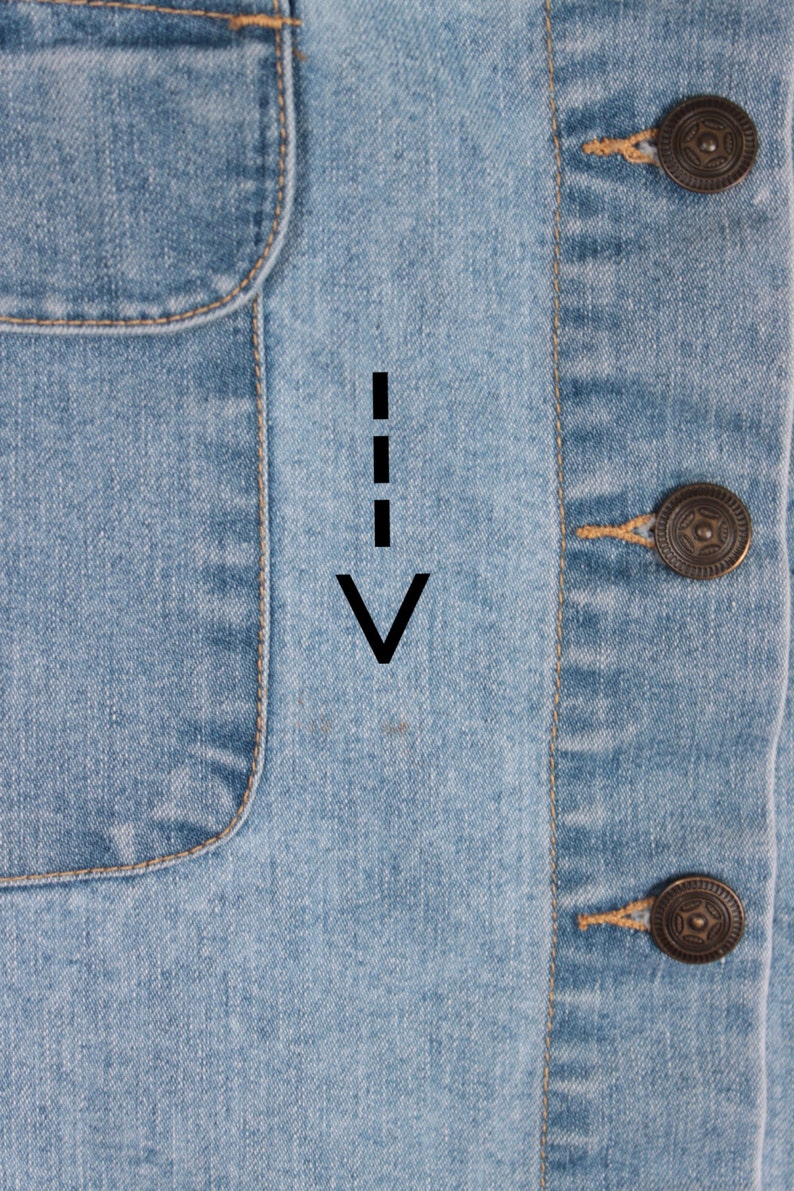 May include: Close-up of a light blue denim jacket with a pocket on the left side and a button closure on the right side. The jacket has a light brown stitching detail.