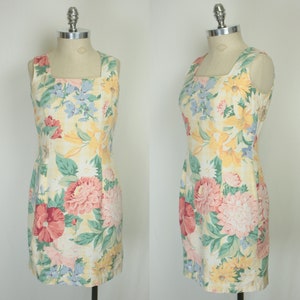 May include: A sleeveless dress with a square neckline and a floral print. The dress is yellow with pink, red, and blue flowers.