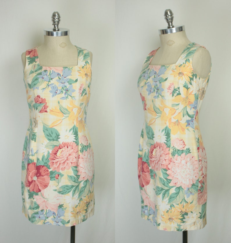 May include: A sleeveless dress with a square neckline and a floral print. The dress is yellow with pink, red, and blue flowers.