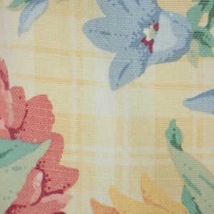 May include: A yellow fabric with a checkered pattern and a floral design. The flowers are pink, blue, and yellow.