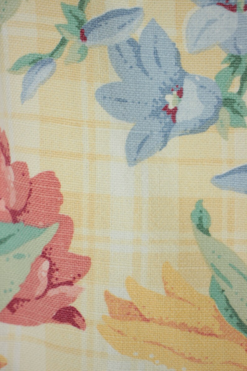 May include: A yellow fabric with a checkered pattern and a floral design. The flowers are pink, blue, and yellow.