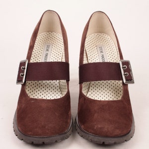 May include: Pair of brown suede Mary Jane style shoes with a strap and buckle closure. The shoes have a chunky sole and a polka dot patterned insole. The brand name "STEVE MADDEN" is printed on the insole.