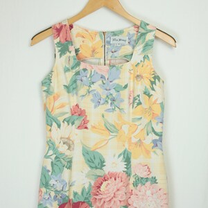May include: A sleeveless yellow floral dress with a square neckline. The dress has a variety of flowers in shades of pink, red, blue, and yellow. The dress is made by the brand "Paris Blues".