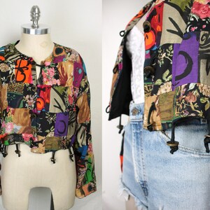 May include: A cropped, multi-colored patchwork jacket with long sleeves and a tie closure at the neck. The jacket is made of a variety of fabrics and patterns, including floral, geometric, and abstract designs.