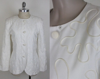 Puede incluir: Una chaqueta blanca con un diseño abstracto único. La chaqueta tiene un cierre de botones en la parte delantera y mangas largas. El diseño se crea con costuras elevadas que crean un efecto 3D.