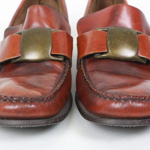 May include: A pair of brown leather loafers with a large metal buckle on each shoe.
