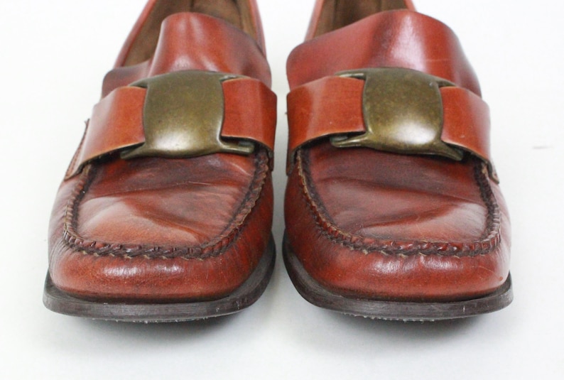 May include: A pair of brown leather loafers with a large metal buckle on each shoe.