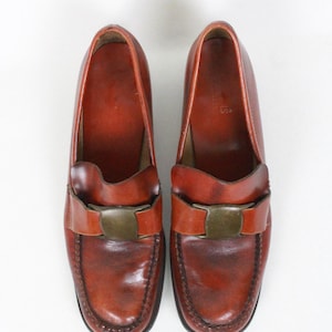 May include: A pair of brown leather loafers with a buckle detail. The loafers have a pointed toe and a low heel.