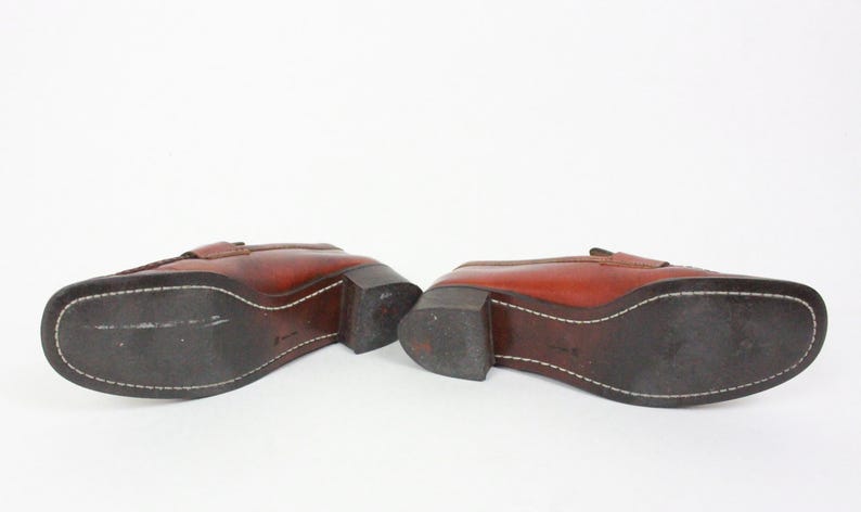 May include: A pair of brown leather loafers with a stitched seam around the sole. The loafers have a low heel and a pointed toe.