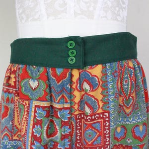 K&ouml;nnte beinhalten: Ein bunter Patchwork-Rock mit einem gr&uuml;nen Bund und vier gr&uuml;nen Kn&ouml;pfen. Der Rock hat verschiedene Muster in Rot-, Blau-, Gelb- und Gr&uuml;nt&ouml;nen.