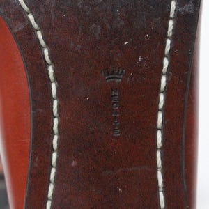 May include: Close-up of the bottom of a brown leather shoe with white stitching around the edge. The shoe has a crown logo and the text "NEOLITE" embossed on the leather.