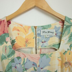 May include: A sleeveless floral dress with a square neckline and a zipper closure in the back. The dress has a yellow, green, pink, and blue floral pattern. The label on the dress reads "Paris Blues" with the size "7" printed below.