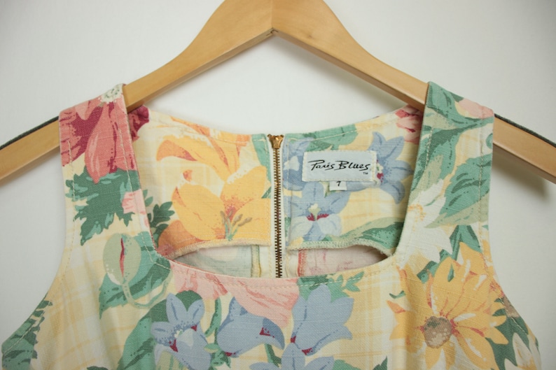 May include: A sleeveless floral dress with a square neckline and a zipper closure in the back. The dress has a yellow, green, pink, and blue floral pattern. The label on the dress reads "Paris Blues" with the size "7" printed below.