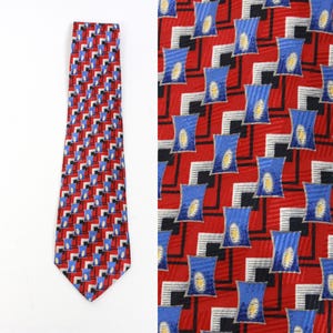 Puede incluir: Una corbata de seda con un patrón geométrico en rojo, azul, blanco y negro. El patrón presenta cuadrados y rectángulos.