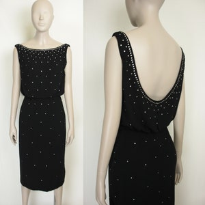 Può includere: Un abito nero con scollatura a barchetta e gonna al ginocchio. L'abito è decorato con abbellimenti argentati sparsi. Anche lo scollo e le spalline sono impreziositi. L'abito è esposto su un manichino.