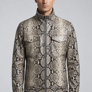 May include: A long-sleeve jacket featuring a grey and black snakeskin pattern. The jacket has a high collar, a full-length central zip, and two chest pockets with button-down flaps. The design includes long sleeves with buttoned cuffs.