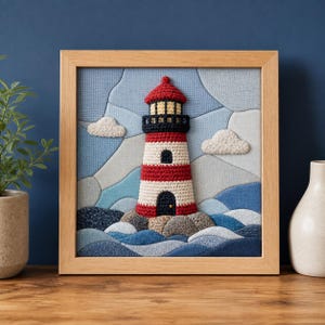 May include: A square framed textile art piece featuring a crocheted lighthouse with red and white stripes, a black lantern room, and a dark door. The lighthouse sits on gray textured rocks amidst blue fabric waves and white clouds.