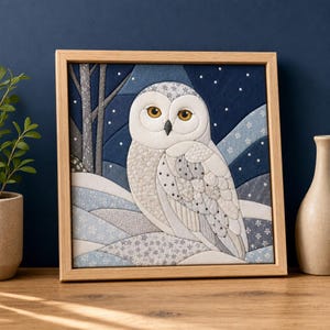 Könnte beinhalten: Ein quadratisches, gerahmtes Stoffkunstwerk mit einer weißen Schnee-Eule mit gelben Augen vor einem dunkelblauen Nachthimmel mit weißen Schneeflocken, stilisierten Bäumen und geschichteten Schneehügeln in hellblauen, grauen und weißen Stoffen.