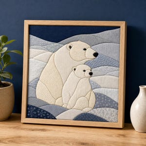 Könnte beinhalten: Ein quadratisches Wandbild aus Stoff in einem hellen Holzrahmen mit einer gesteppten Applikation eines großen Eisbären und eines kleinen Jungtiers. Die cremefarbenen Bären sind vor einem Hintergrund aus blauen, grauen und weißen Stoffen.