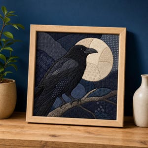 May include: A square framed fabric art piece featuring a quilted black crow perched on a branch against a dark blue landscape and a large, pale circular moon. The artwork uses various shades of blue and grey fabric textures and patterns.