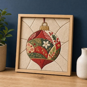 May include: A square framed fabric wall art piece featuring a central embroidered Christmas ornament design. The ornament is composed of red, green, and cream fabric segments with floral and berry patterns, set against a beige background.