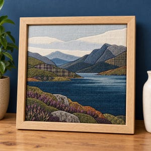 Puede incluir: Una pieza de arte textil rectangular enmarcada en madera clara, que representa un paisaje con un lago azul profundo, colinas onduladas en tonos verdes y marrones a cuadros, brezo morado en primer plano y montañas azules bajo un cielo pálido.