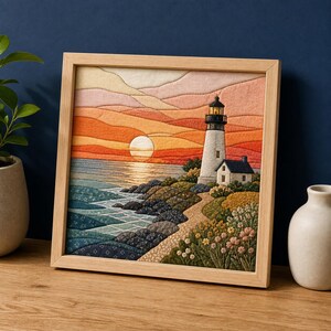 May include: A square fabric wall art piece in a light wood frame depicting a coastal scene with a lighthouse, a sunset, and a rocky shoreline. The textile artwork features layered fabric patches in shades of orange, pink, blue, and green.