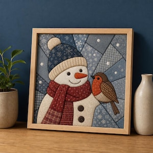 Könnte beinhalten: Ein quadratisches, gerahmtes Wandbild aus Stoff, das einen Schneemann mit einer dunkelblauen Strickmütze und einem roten gemusterten Schal zeigt, mit einer orangefarbenen Karottennase und zwei dunklen Knöpfen. Ein kleines braunes Rotkehlchen sitzt darauf.