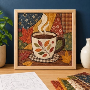 Könnte beinhalten: Ein quadratisches Wandbild aus Stoff in einem hellen Holzrahmen mit einem gesteppten Motiv einer Kaffeetasse mit Dampf, umgeben von herbstlichen Blättern in Rot-, Orange- und Gelbtönen vor einem Patchwork-Hintergrund aus gemusterten Stoffen.