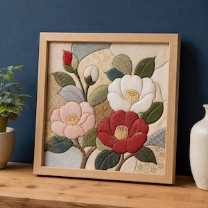 Könnte beinhalten: Ein quadratisches Wandbild aus Stoff in einem Holzrahmen mit einem gesteppten Applikationsdesign aus Kamelienblüten in Rot-, Weiß- und zarten Rosatönen. Die Komposition umfasst grüne Blätter, Knospen und einen strukturierten Hintergrund.