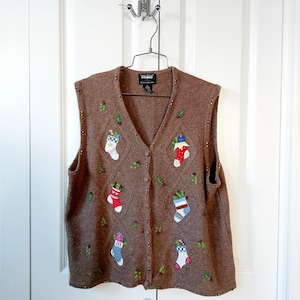 May include: Brown sleeveless sweater with a V-neck, decorated with Christmas stocking appliqués in various colors. The sweater has a button-down front and small green leaf and bead accents.