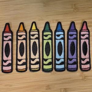 Puede incluir: Siete parches de crayones coloridos en fila, cada uno con un color diferente: rojo, naranja, amarillo, verde, azul, morado y rosa. Los parches tienen un óvalo negro en el centro y están bordados con un diseño detallado.