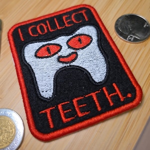 May include: A rectangular embroidered patch with a black background and a red border. It features a white tooth character with red eyes and a red mouth. The text "I COLLECT" is embroidered in red above the tooth and "TEETH." below it.