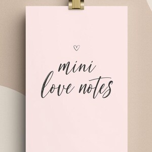 May include: A pale pink card with the words "mini love notes" in black script, held by a gold-coloured clip. A small heart is above the text. The background is a neutral beige colour.