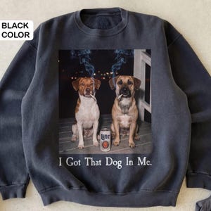 May include: Black sweatshirt with a graphic of two dogs smoking cigarettes, a beer can, and the text "I Got That Dog In Me." The dogs are brown and white, and tan. The beer can is white and orange.
