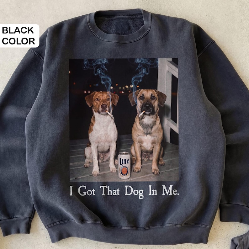 May include: Black sweatshirt with a graphic of two dogs smoking cigarettes, a beer can, and the text "I Got That Dog In Me." The dogs are brown and white, and tan. The beer can is white and orange.
