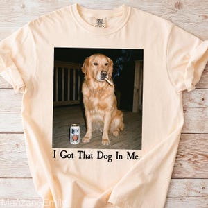 Puede incluir: Camiseta color crema con una imagen humor&iacute;stica de un Golden Retriever con un cigarrillo y una lata de cerveza. El texto "I Got That Dog In Me" est&aacute; impreso debajo. La camiseta es de un material suave.