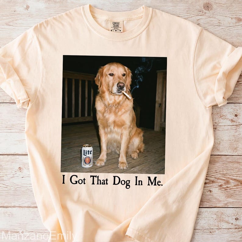 Puede incluir: Camiseta color crema con una imagen humor&iacute;stica de un Golden Retriever con un cigarrillo y una lata de cerveza. El texto "I Got That Dog In Me" est&aacute; impreso debajo. La camiseta es de un material suave.