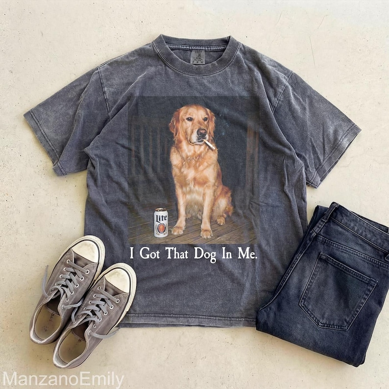 Puede incluir: Camiseta gris carb&oacute;n con un golden retriever fumando un cigarrillo y una lata de cerveza. El texto "I Got That Dog In Me" est&aacute; impreso debajo. La camiseta se combina con zapatillas grises y vaqueros oscuros.