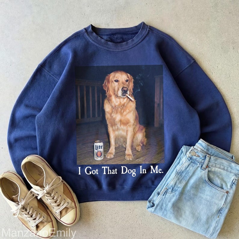 Puede incluir: Sudadera azul marino con un gr&aacute;fico de un golden retriever fumando un cigarrillo y una lata de cerveza. El texto "I Got That Dog In Me" est&aacute; debajo del gr&aacute;fico. Tambi&eacute;n se ven unos vaqueros azul claro y zapatillas de lona.