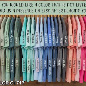 Puede incluir: Una exhibici&oacute;n de camisetas Comfort Color C1717 en varios colores, desde blanco hasta marfil y negro. Cada camiseta cuelga de un estante de madera con etiquetas de color. El texto en la parte superior dice: "SI DESEA UN COLOR QUE NO EST&Aacute; EN LA LISTA, ENV&Iacute;ENOS UN MENSAJE EN ETSY DESPU&Eacute;S DE REALIZAR SU PEDIDO."