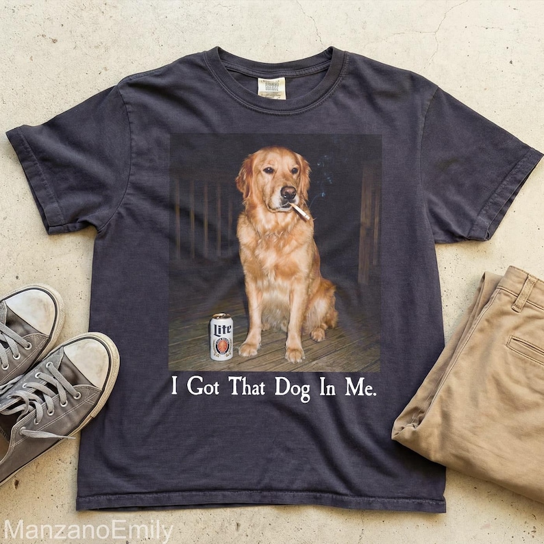 Puede incluir: Camiseta gris oscuro con un gr&aacute;fico de un Golden Retriever fumando un cigarrillo y una lata de cerveza. El texto "I Got That Dog In Me" est&aacute; impreso debajo. Tambi&eacute;n se ve un par de zapatillas grises y pantalones color caqui.