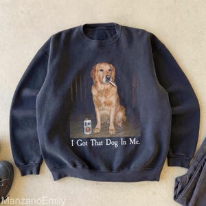 Puede incluir: Sudadera gris oscuro con un dise&ntilde;o de un golden retriever fumando un cigarrillo, con una lata de cerveza al lado. El texto "I Got That Dog In Me" est&aacute; impreso debajo. La sudadera es de estilo casual.