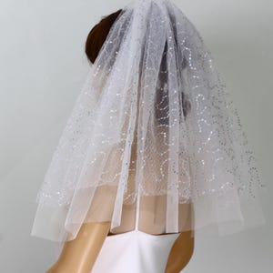 May include: A white bridal veil with a two-tier design. The tulle veil is adorned with scattered silver sequins, creating a sparkling effect. The veil is a classic accessory for weddings and special occasions.