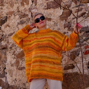 May include: A cozy, oversized sweater in shades of yellow, orange, and brown. The sweater features a high neckline and long sleeves. The knitted garment has horizontal stripes and a relaxed fit, perfect for cooler weather.