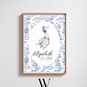 May include: A framed print featuring a watercolor illustration of a goose wearing a blue bonnet and scarf, with the name "Elizabeth Claire" below. The background has a blue floral pattern, and the frame is light brown. The Wallace Stitch Co. logo is at the bottom.