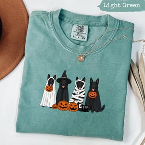 Light green t-shirt with four dogs in Halloween costumes and pumpkins.