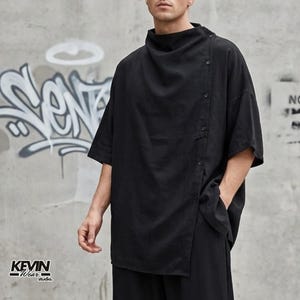 Può includere: Camicia nera a maniche corte con un'esclusiva chiusura asimmetrica con bottoni e collo alto. La camicia ha una vestibilità ampia ed è realizzata in un tessuto morbido e fluido. La camicia fa parte di una collezione streetwear.