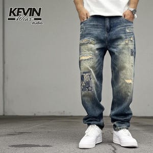 May include: Blue denim jeans with distressed details and patchwork accents. The jeans have a relaxed fit and are paired with white trainers. The text "KEVIN Wear studio" is visible in the upper left corner.