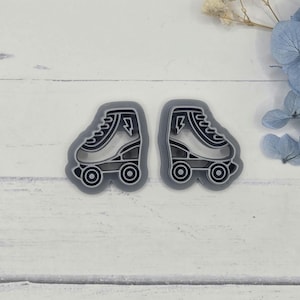 May include: Two gray roller skate cookie cutters. Each cutter features a detailed outline of a roller skate with wheels and a lightning bolt design. The cutters are made of plastic and are designed for baking or crafting.